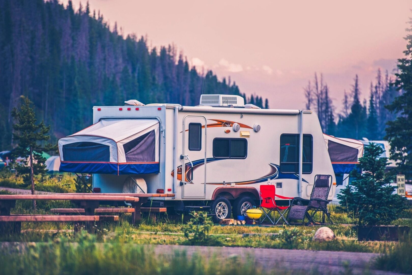 fm=f_1415 A white camper parked in the grass near trees.